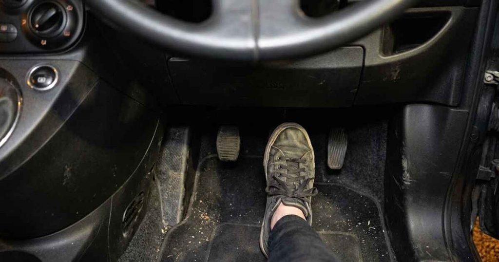 Driver pressing the brake pedal firmly inside a Fiat 500 to check for normal feel after the ABS warning light came on, footwell view showing worn pedals and dark grey carpet