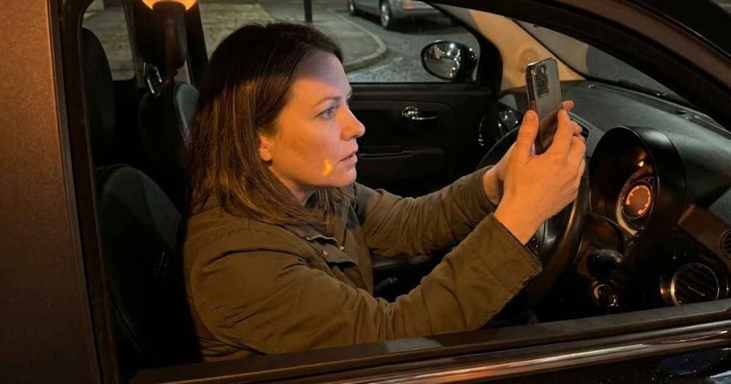 Woman photographing the amber triangle warning light on a Fiat 500 instrument cluster with her smartphone while sitting in the driver seat at night