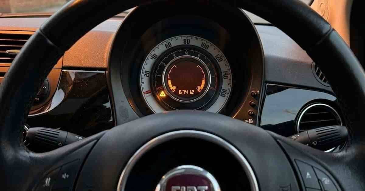 Amber triangle warning light glowing alone on a 2014 Fiat 500 Lounge instrument cluster at night with all other lights off