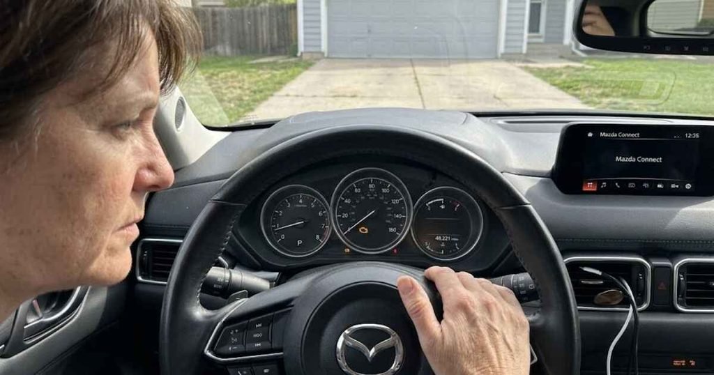 Driver checking a steady Mazda check engine light on the dashboard